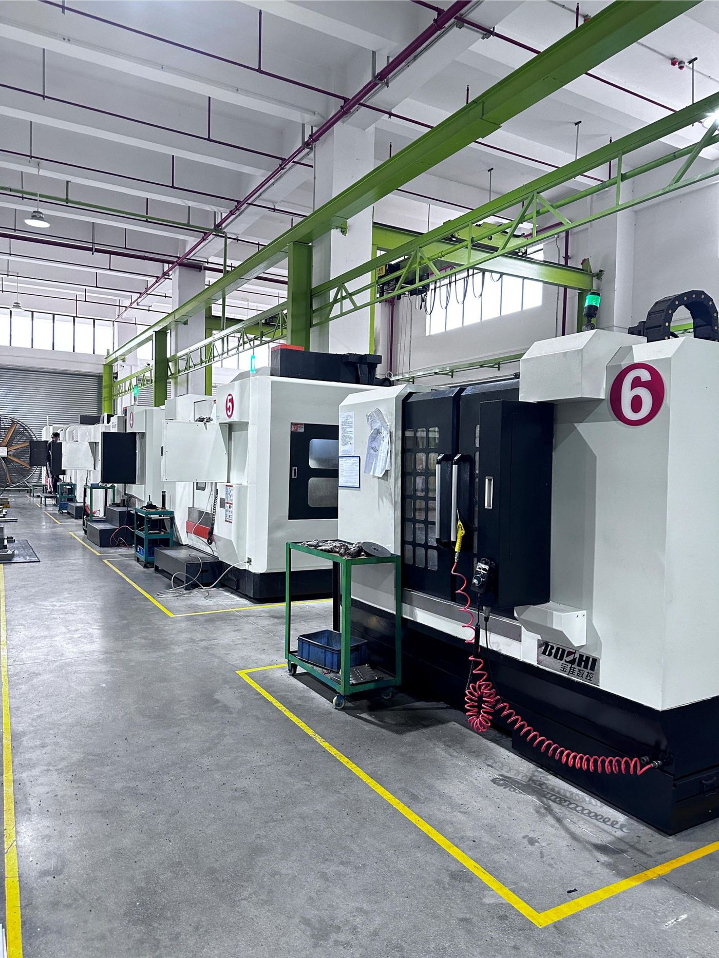 Row of numbered CNC machining centres in the tooling hall, served by overhead jib cranes